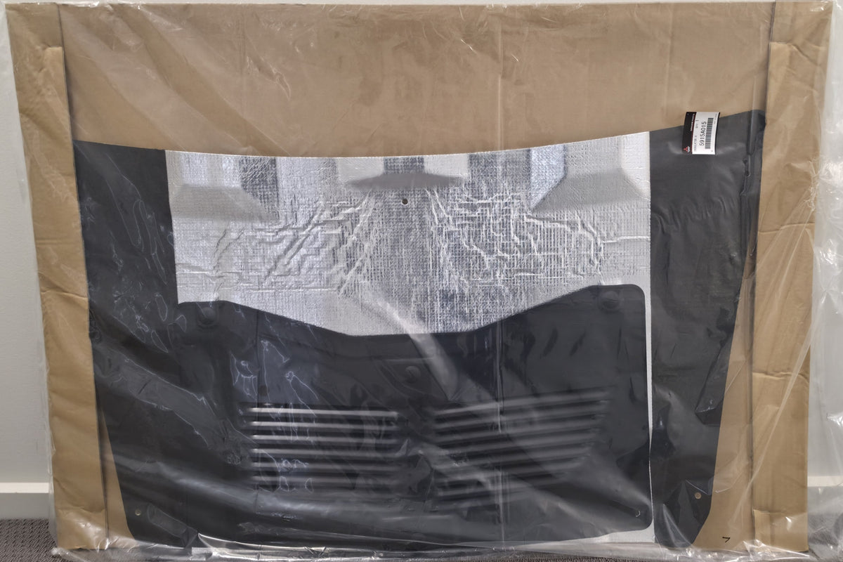 A black car grille surround with a vented lower section, wrapped in clear plastic and held in place by brown cardboard sheets, photographed against a plain indoor wall.
